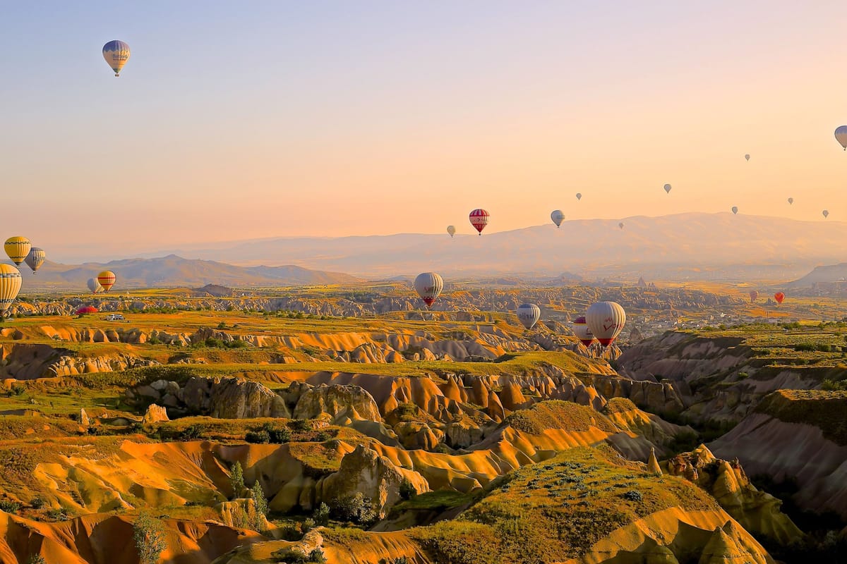 Des dizaines de montgolfières colorées flottent dans un ciel orangé au lever du soleil, au-dessus des vallées de roche ocre et des cheminées de fée de Cappadoce.